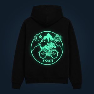 Back view of a black hoodie featuring a glowing turquoise circular emblem with mountains, sun, moon, stars and a cyclist; includes the year 1943.