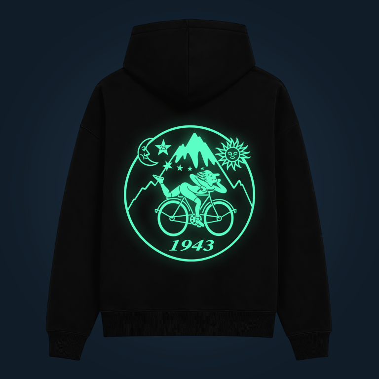 Back view of a black hoodie featuring a glowing turquoise circular emblem with mountains, sun, moon, stars and a cyclist; includes the year 1943.